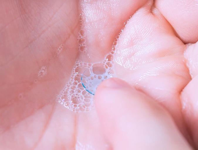 Contactlens op vingertop bij de wastafel